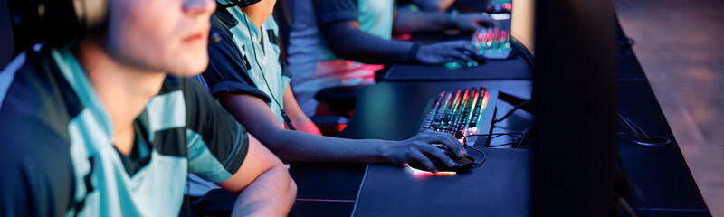 Selective focus on gamers hands using brightly lit keyboards while playing in competitive game in cyber games arena club