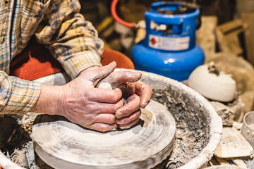 Muscular hands of middle-aged man, potter, soiled in clay, form pottery from clay on potter's wheel