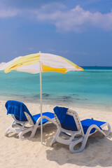 Two Blue Plastic Chaise Lounges under Yellow Umbrella on the Local Bikini Beach of the Maafushi Island, Maldives