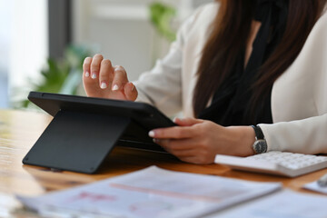 Fototapeta premium Close up woman’s hand using a tablet and calculator in the office and working on data, charts and documents on the table, for finance and technology concept.