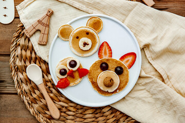 Pancakes With Funny Faces Decorated For Kids. Healthy Fruit Pancakes For baby Meal over wooden background, top view