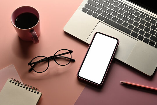 Top view sweet color flat lays of a cup of coffee, note book, pencil, smartphone ,glasses and laptop on a pink background , for business and technology concept.