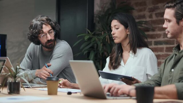 Video of casual multiethnic business people working with laptops and digital tablets while talking of they new project together in the coworking.