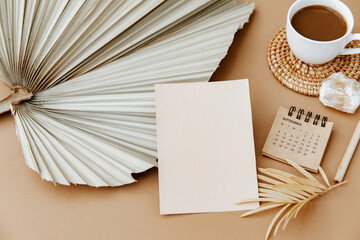 Aesthetic theme. Blank paper sheet card with mockup copy space, coffee cup, dry palm leaf on neutral background. Minimal business brand template. Flat lay, top view