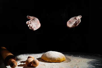 women kneads dough and scatters flour on a black background.