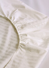 Corner of the sheet with sewn-in elastic band for a good fit on the mattress and a comfortable sleep. White fabric for mockup overlay design. Home textiles for the bedroom. Linen in stripe satin 