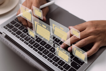 Paperless workplace idea based on e-documents. On a virtual screen, a businessman works on a laptop computer keyboard with electronic document icons.