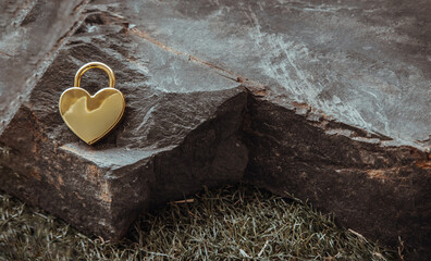 Golden heart shaped love padlock on Huge stone over grass background. Valentine's day concept, Copy...