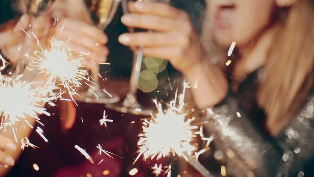 Close up portrait of friends at party celebrating birthday, drinking champagne or sparkling wine, pouring into glass, smiling, laughing, holding and waving sparkler. Happiness or fun concept.