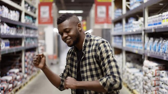 Smiling guy dances gesturing in hardware goods store between stacks slow motion
