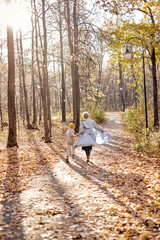 Fototapeta premium Rear view on cheerful mother and child boy having fun in autumn park, running, having rest. friendly family in casual clothes walking, spending time together, at summer day. view from back