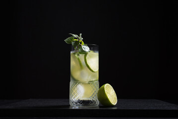 Un vaso de refrescante cóctel  de jugo de lima con rodajas de lima y hielo sobre fondo negro	