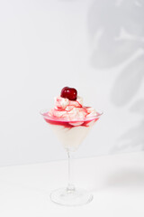 Helado de crema con jarabe de cereza y cereza sobre una mesa blanca. Sombras suaves de hojas en la pared postre de verano