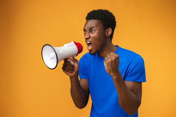 Young black man shouting in megaphone on yellow background