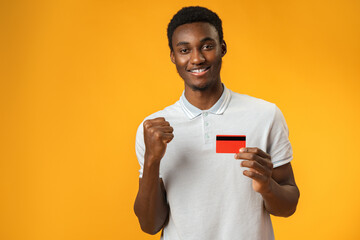 Afro american man holding red credit card against yellow background in studio