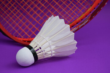 White cream badminton shuttlecock  in front of badminton rackets on purple floor of indoor badminton court, soft and selective focus on shuttlecock, concept for badminton sport lovers around the world