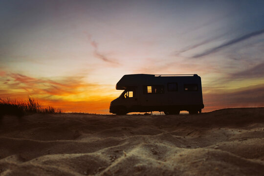 Sunset and caravan silhouette. Van life concept. Travelling in the Europe. Camper van on the beach.