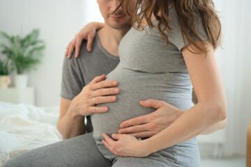 Pregnant woman and her husband holding hand together. Young family is happy in anticipation of a baby, parenthood. Two hands holding baby inside a pregnant woman
