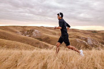 fitness runner man in black tracksuit running on field training for marathon run doing high...