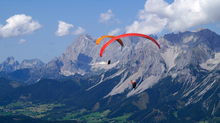 friends paragliding over the vast alpine valley surrounded by the scenic high Austrian Alps of the...