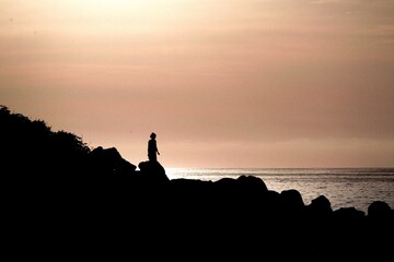 Silueta de niña pequeña juega a tirar piedras en un acantilado junto al mar