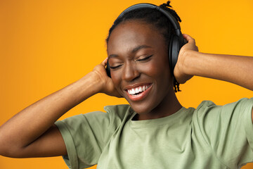 Happy young Afro American woman listening to music in headphones against yellow background