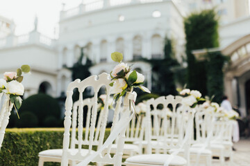 White chairs with white flowers decoration on the lawn near the luxury restaurant for wedding ceremony.