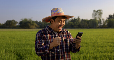 Happy Asian farmer man looking to smartphone display screen with glad wow surprise face at green rice field.