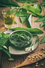 Homemade wild garlic pesto in a glass bowl on wooden background, decorated with leaves, parmesan cheese and olive oil, desaturated colors, vertical
