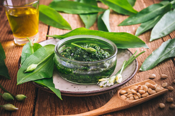 Homemade wild garlic pesto in a glass bowl on wooden background, decorated with leaves, parmesan...