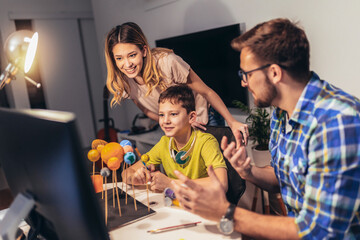 Happy school boy and his parent making a solar system for a school science project at home