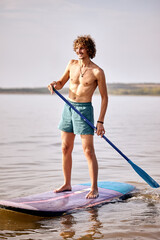 shirtless young caucasian male standing on surfboard in river, concentrated. man during active surfing training alone. Surfing, subsurfing, active sport concept