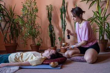 a young woman conducts a session to a client with Tibetan bowls