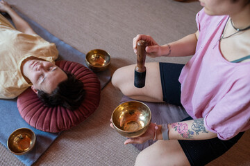 a young woman conducts a session to a client with Tibetan bowls
