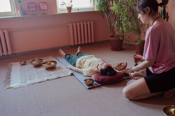 a young woman conducts a session to a client with Tibetan bowls