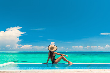 Obraz premium Luxury summer vacation tourist woman relaxing by swimming pool. Elegant lady relaxing sunbathing enjoying travel holidays at resort infinity overwater pool. Luxury lifestyle.