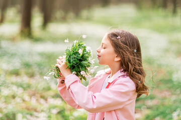 portrait of a girl with primroses. A child in the spring forest sniffs a bouquet of flowers.