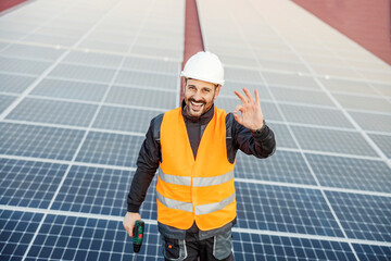 A happy worker finished successfully solar panels installing and giving okay gesture for renewable...