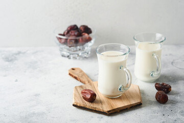 Ramadan Kareem food and drinks. Plate of dates, glass of milk and date palm branch on light grey background. Righteous Muslim Lifestyle. Place for text. Selective focus.