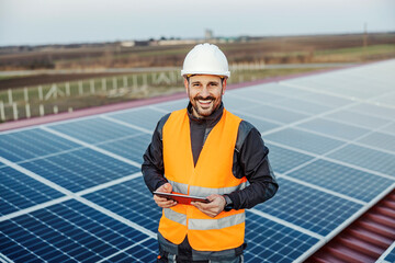 A handyman holding tablet for checking on solar panels and smiling at the camera.