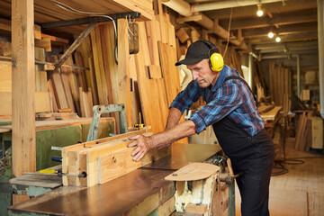 Senior carpenter in uniform works on a woodworking machine at the carpentry manufacturing