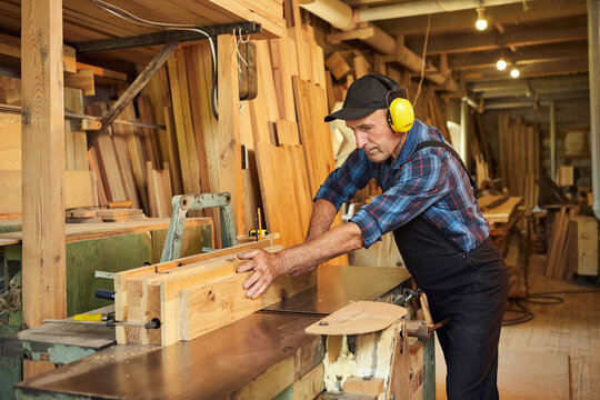 Senior carpenter in uniform works on a woodworking machine at the carpentry manufacturing