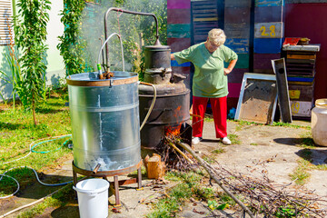 Woman is manually mixing fruit marc in distillation apparatus for making domestic alcohol liquor