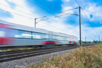 Close up of a train with overhead electrification speeding through English countryside with motion...