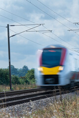 Close up of an express train with overhead electrification speeding through English countryside with motion blur - 493062157