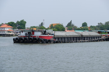 The large cargo boat which loads a lot of sand is cruising along the large river.