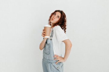 Cheerful redhead girl, wearing denim dungarees and white t-shirt, feeling energetic after drinking coffee, ready to conquer the world over white background