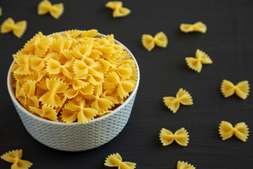 Raw Organic Farfalle Pasta in a Bowl on a black background, side view.