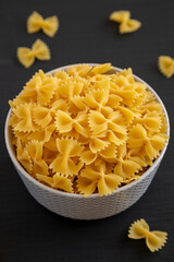 Raw Organic Farfalle Pasta in a Bowl on a black surface, side view.