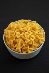 Raw Organic Farfalle Pasta in a Bowl on a black background, low angle view.